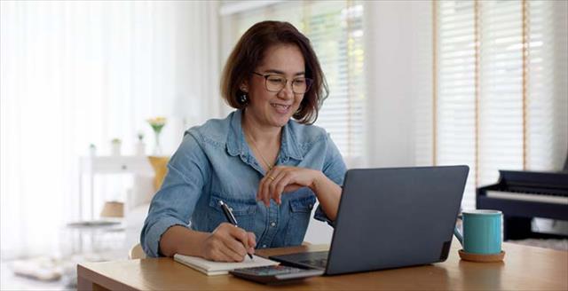 An adult woman, looking enviably cool and casual, takes notes while working on a laptop