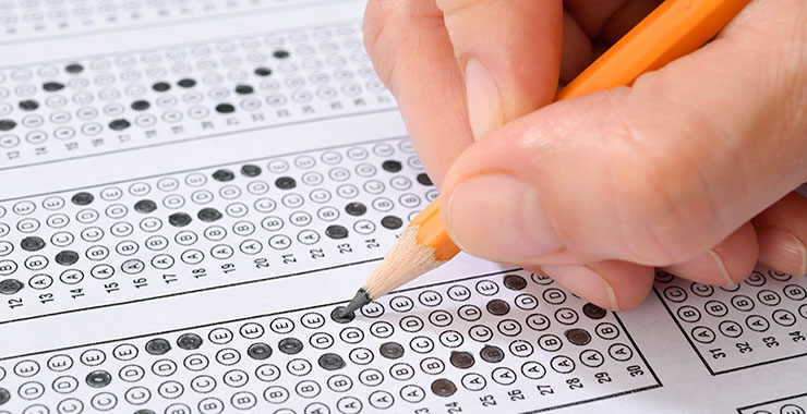 Hand holding pencil fills in scantron exam sheet.