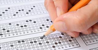 Hand holding pencil fills in scantron exam sheet.