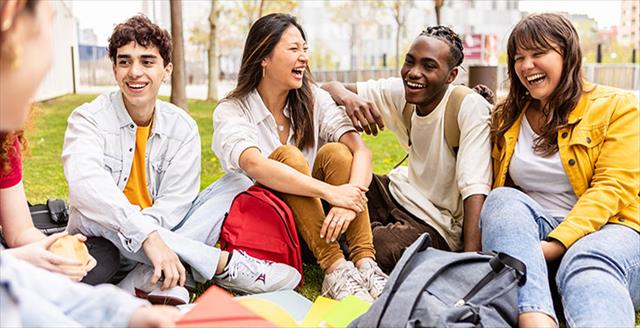 Diverse group of high school-aged students hanging out together outside of school building.