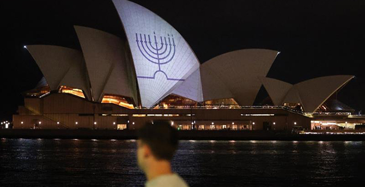 Man walks by Sydney Opera House, which is illuminated with a blue menorah to honor the victims of the Bondi Beach shooting.