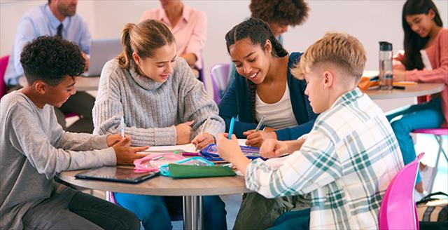 Diverse group of high school-aged students sit together at a table working on a project.