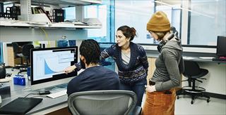 two people pointing at something on a computer monitor