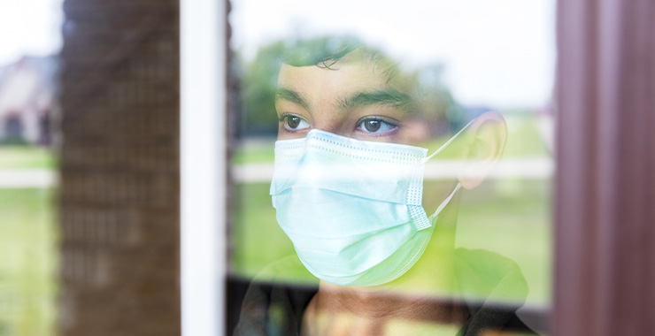 young person wearing a non medical mask as he stares out a window