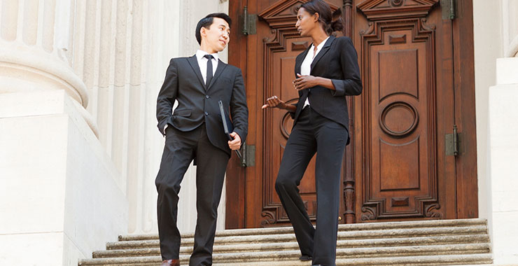 Two well-dressed professionals walk down courthouse steps.