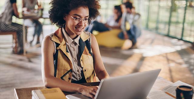 Young, African American woman sits at desk while typing on laptop.