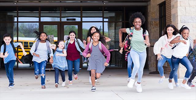 Diverse group of children bursting through the school doors to leave for the day.