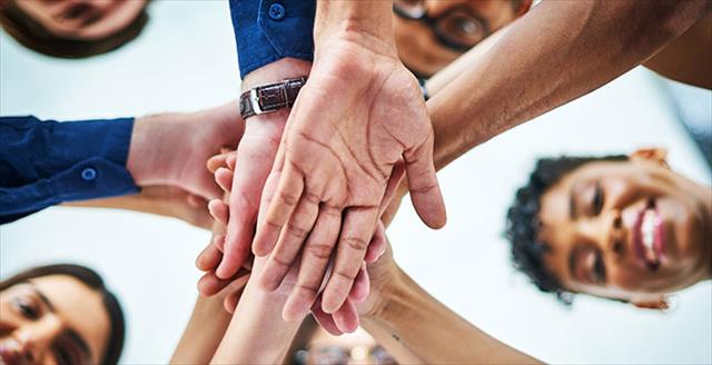 Group of five multicultural people stand in a circle and put their hands in the center.
