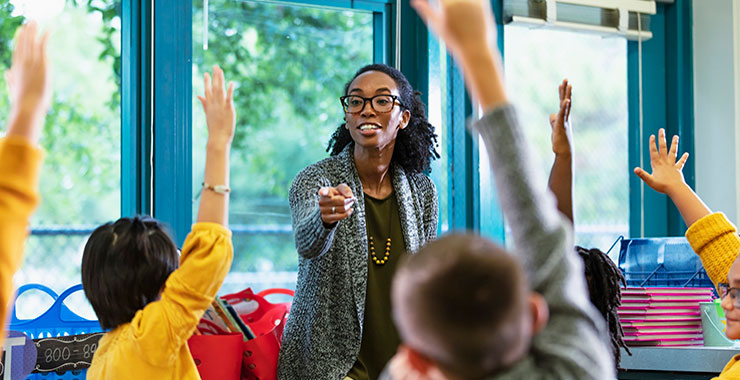 eacher in classroom points to student raising hand.