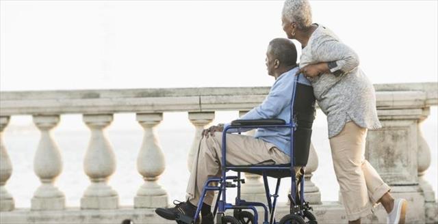 Smiling man in wheelchair with partner crossing a bridge.