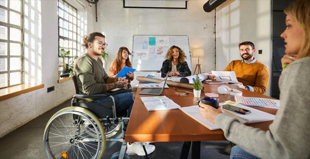 Smiling man in wheelchair communicating with his colleagues during a meeting at casual office
