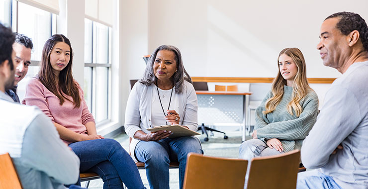 African American therapist leads diverse group of patients in group therapy session.