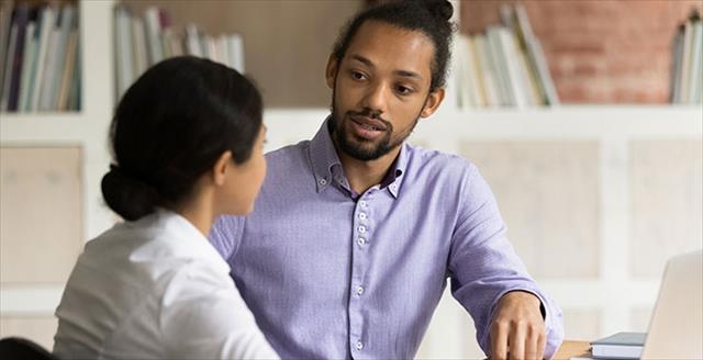 Two young professionals sit at a table talking with each other.