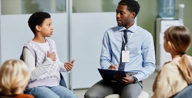 Young African American psychologist hosts group therapy session for children.