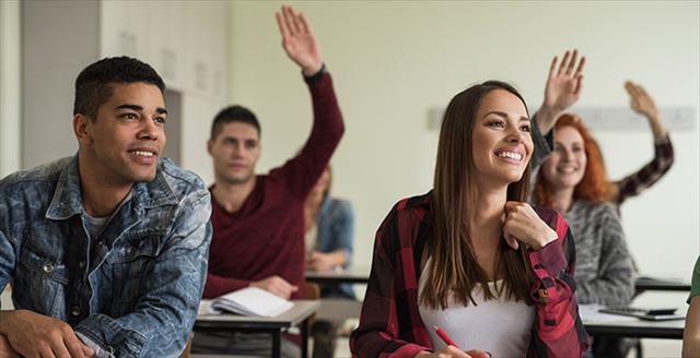 College students seated in classroom smiling, with hands raised.
