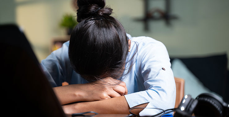 Young academic professional cradles head in arms on desk.