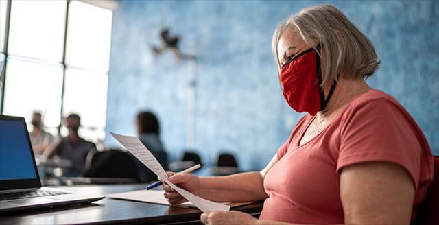 Female teacher grading educational exam—wearing face mask