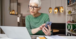 person reviewing notebook computer screen and mobile phone