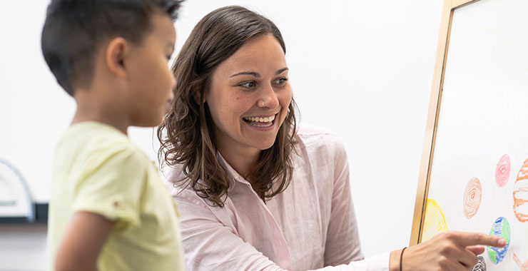 Teacher points to white board while assisting student.
