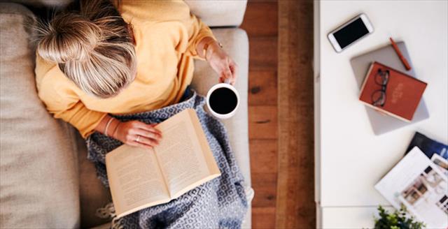 Girl reading book at home holding coffee cup