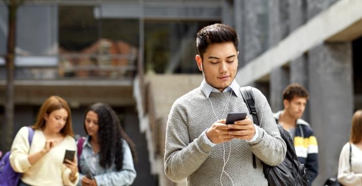 Young male student with walking outside looking at his phone