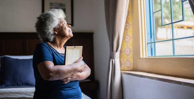 Senior woman holding a picture frame missing someone at home