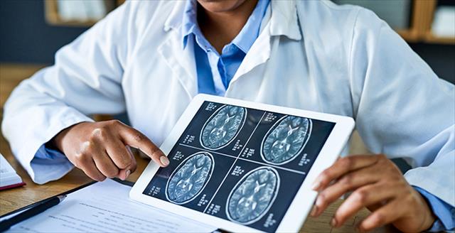 Hands holding a tablet and showing brain scans across a desk