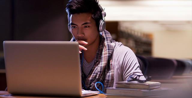 Young Asian man using laptop while wearing headphones in the library.