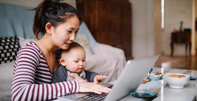 New parent works at laptop while holding baby