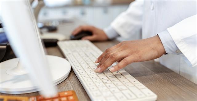 Closeup of pharmacist's hands typing on a computer keyboard at the pharmacy counter