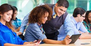Smiling teacher and female student looking at tablet