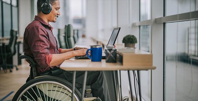 Professional man in a wheelchair sitting at a long desk and working on a laptop