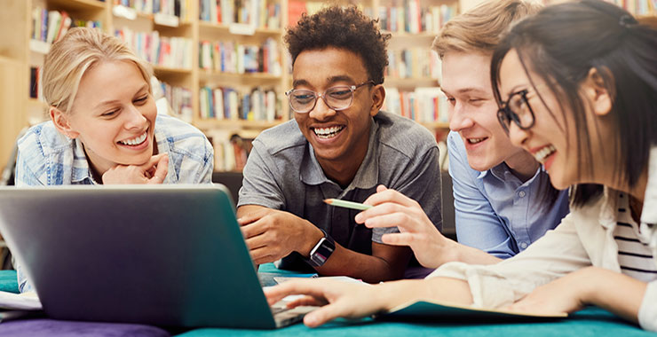 Diverse group of smiling high school students lying on floor in campus library and laughing.