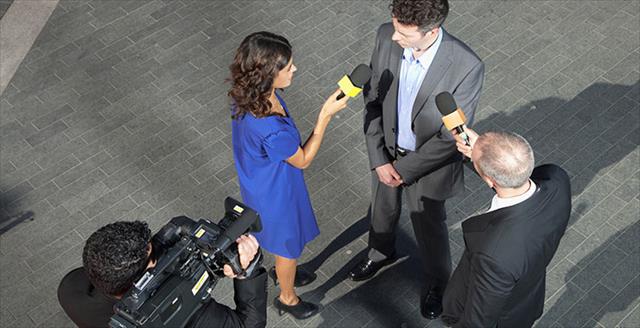 Group of reporters holding microphones interview a man