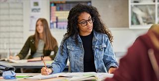 African American girl reading and taking notes during a lesson in classroom.