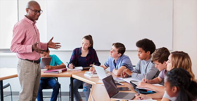 African American teacher delivers presentation in front of students in classroom.