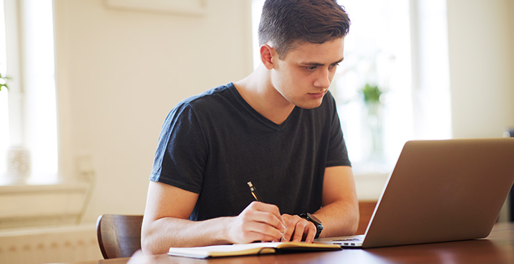 Student using laptop and writing notes