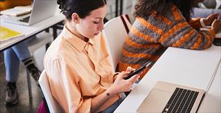 Young female college student texting on her phone during class.