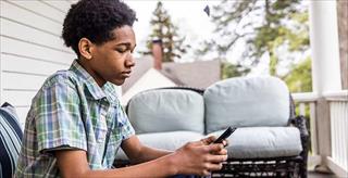 Adolescent sitting on a porch and looking at a smartphone.