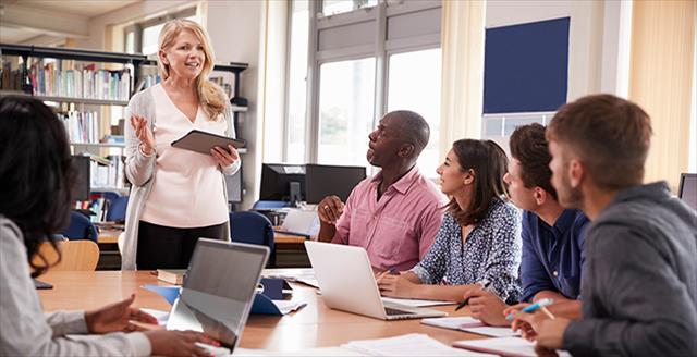 Teacher holding an iPad leading group discussion among other teachers.