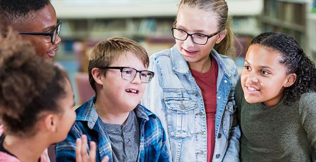 Diverse group of middle school-aged students in the library, including one student with a neurodevelopmental disability.