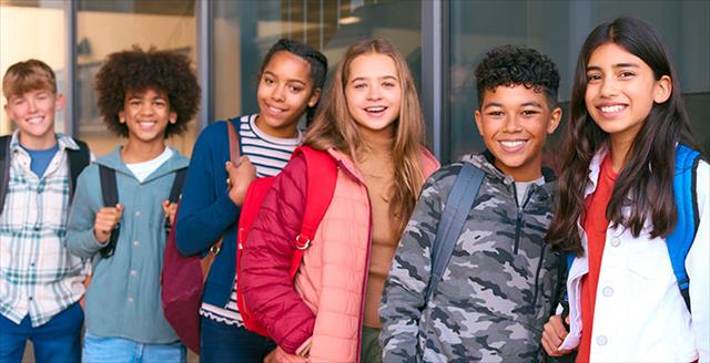 Group of middle school students representing diverse racial and ethnic backgrounds wait in line outside of school building.