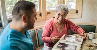 Senior woman and mid adult nurse looking at photo album in the dining room in a nursing home