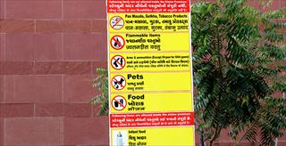 Yellow sign listing prohibited and allowed items with a brick wall in the background and a small tree