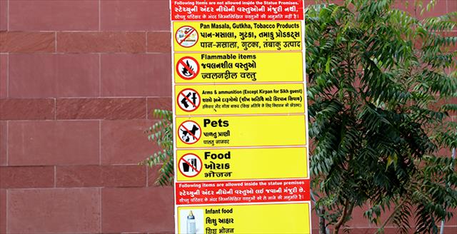 Yellow sign listing prohibited and allowed items with a brick wall in the background and a small tree