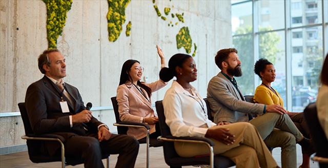 Businesswoman raising hand to ask question during a conference meeting with a world map made of moss in the background, promoting sustainability and global awareness