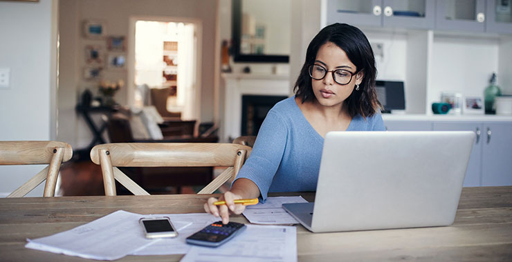 Woman using a calculator while looking at her laptop screen.