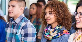 African American college-aged girl wearing colorful scarf sitting next to a Hispanic man.