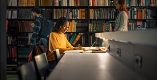 Student sitting in a library working and taking notes
