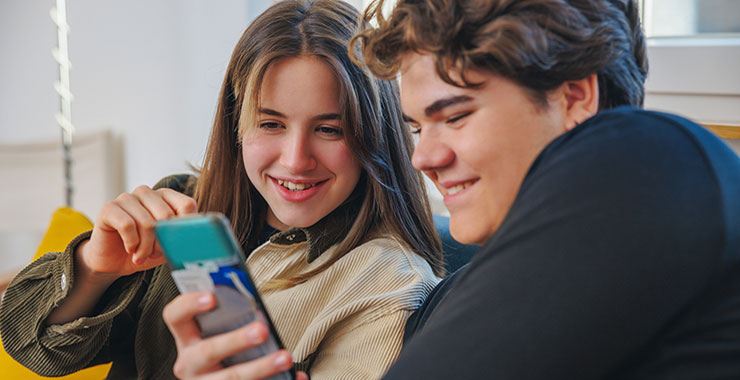 Two teenagers point and laugh at smart phone screen.
